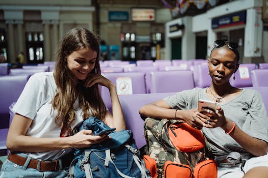 Two women sitting and using smartphones in a station seating area.