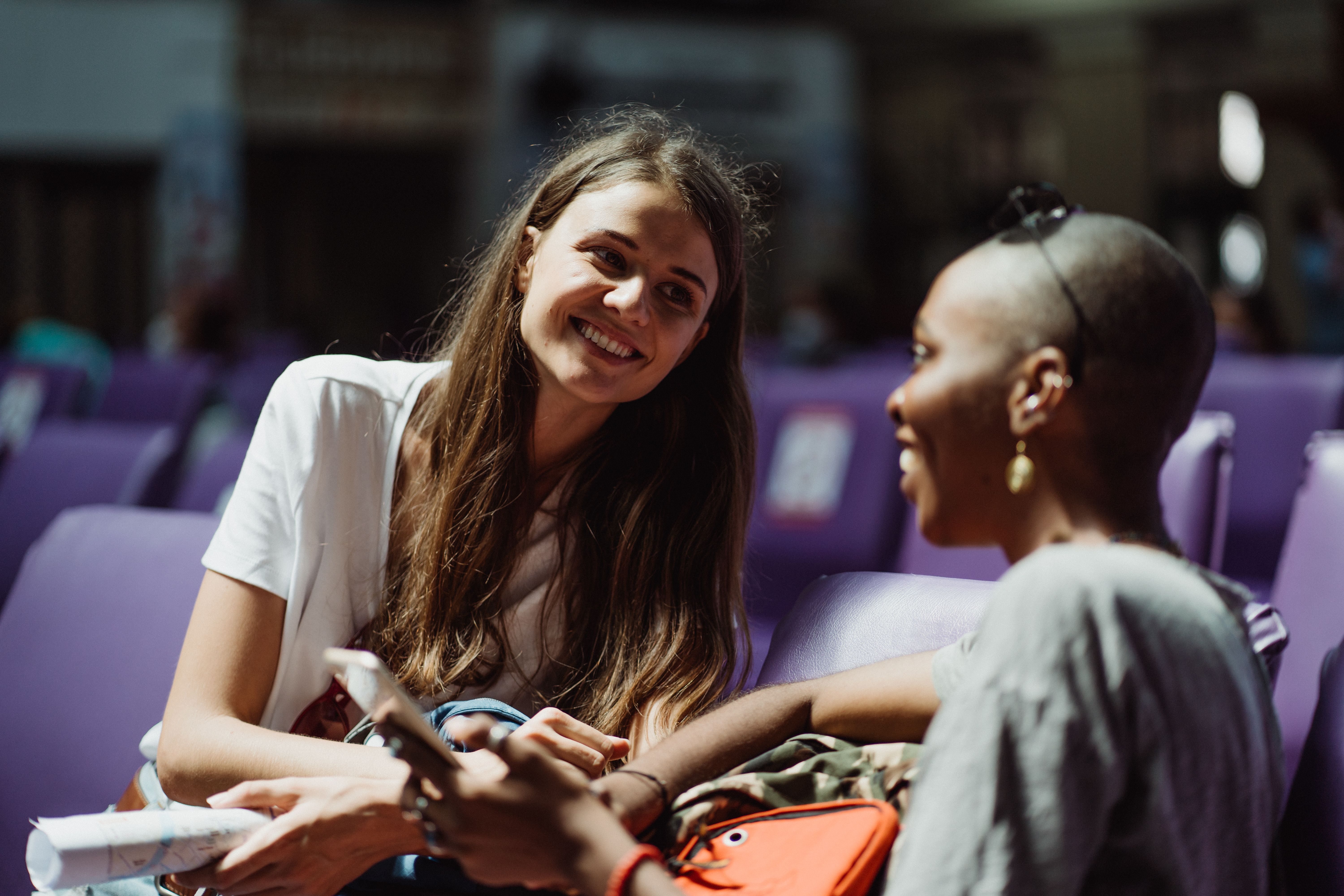 Two women enjoying a friendly conversation while sitting in a vibrant waiting area.