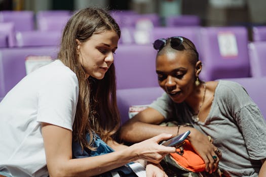 在公共等候区，两名成年女性坐在紫色的座位上，共享一部智能手机