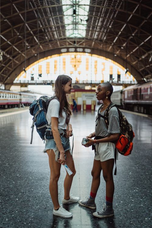Free Two young women with backpacks converse in a train station, capturing travel vibes. Stock Photo