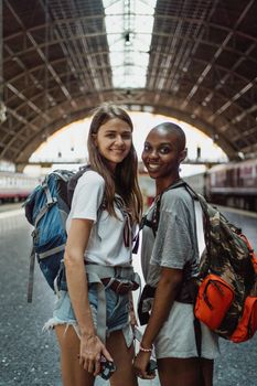 Two backpackers smiling at a train station, ready for travel adventure.