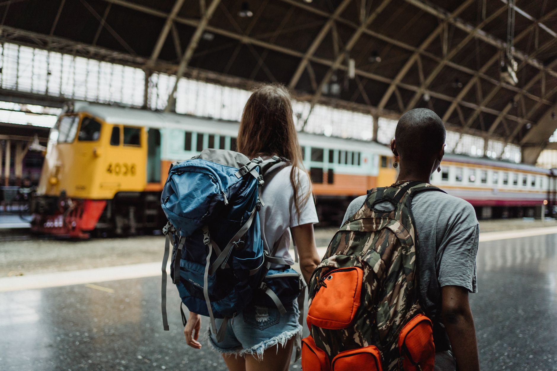 Two travelers with backpacks at a train station platform, ready for their journey.