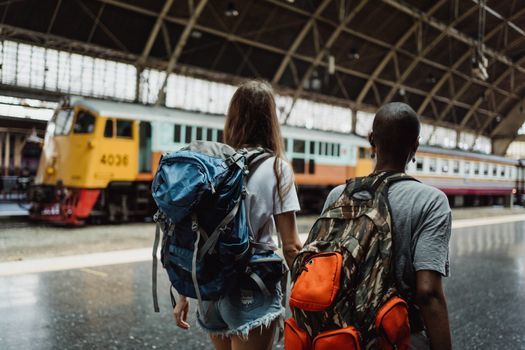 Two travelers with backpacks at a train station platform, ready for their journey.