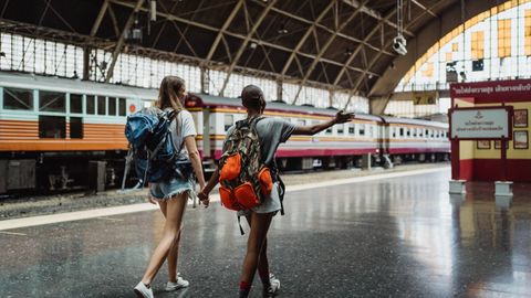 Two women with backpacks walking through a train station, showcasing adventure and friendship.