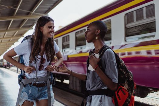 Two backpackers engage in friendly conversation at a railway station, with a train in the background.