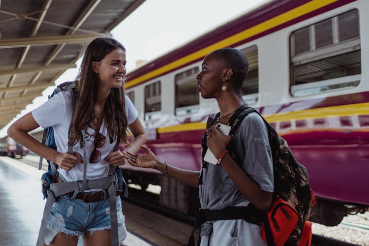 Happy Girls Travelers With Backpacks At Railway Station