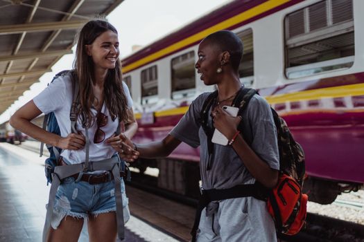 Two women smiling and talking while waiting at a vibrant train station.