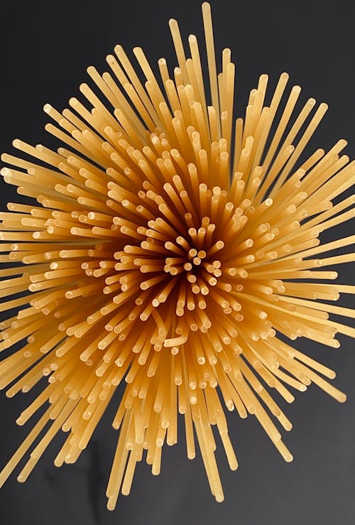 Overhead view of bunch of uncooked golden crunchy thin Italian pasta on dark background