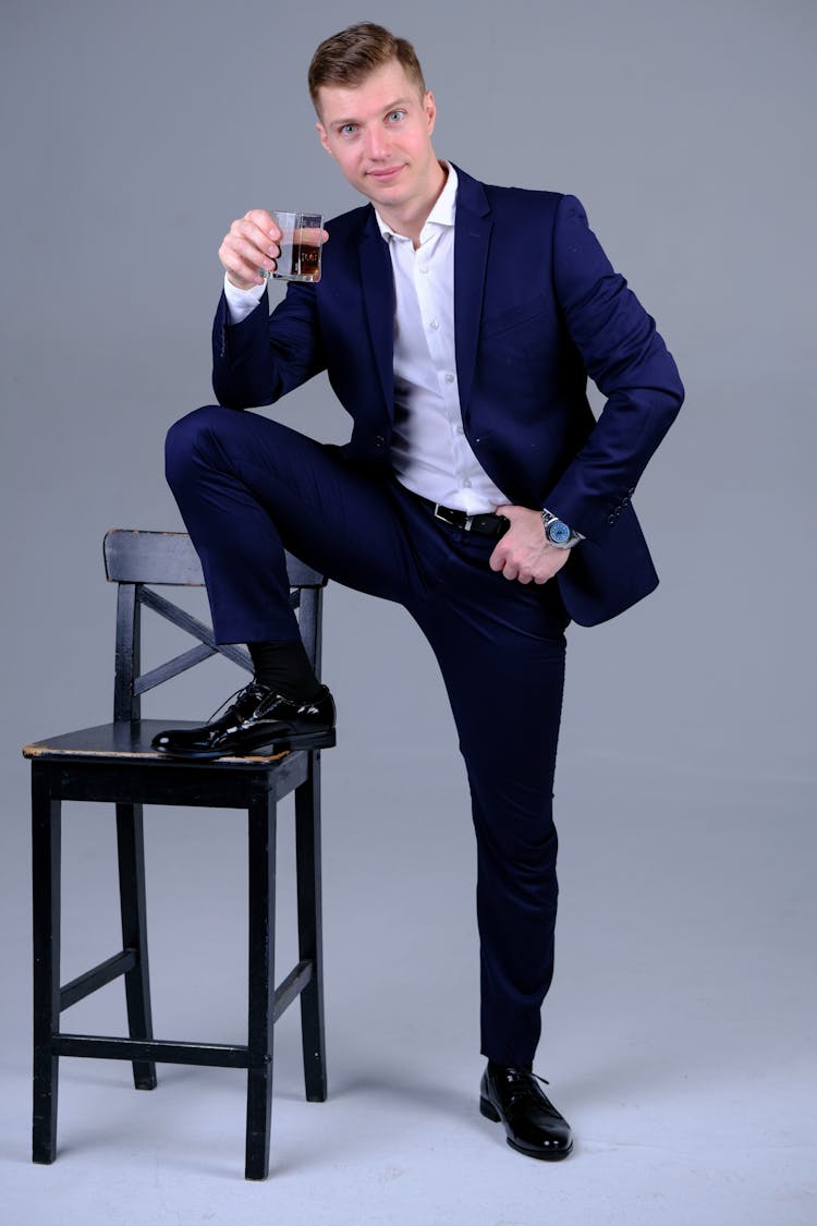 Positive Young Guy In Suit Drinking Alcohol In Studio