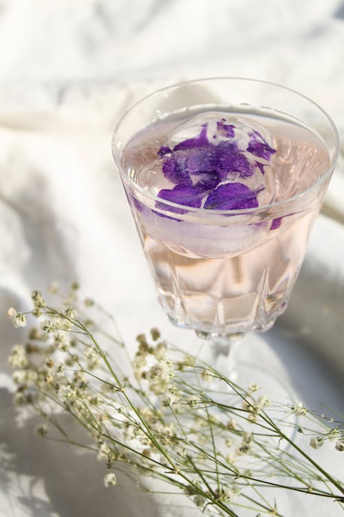 Ice with Purple Flower Petals in a Glass Beside White Flowers