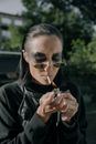 一位女士在户外点燃一支香烟，她留着光滑的头发，体现了赛博朋克风格