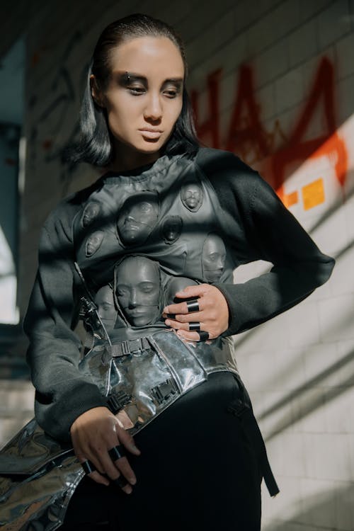 Femme En Veste En Cuir Noir Et Jeans En Denim Noir Assis Sur Un Mur De Béton Blanc