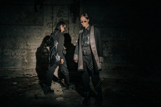 Two models in futuristic fashion pose in a dimly lit urban setting, exuding a cyberpunk vibe.