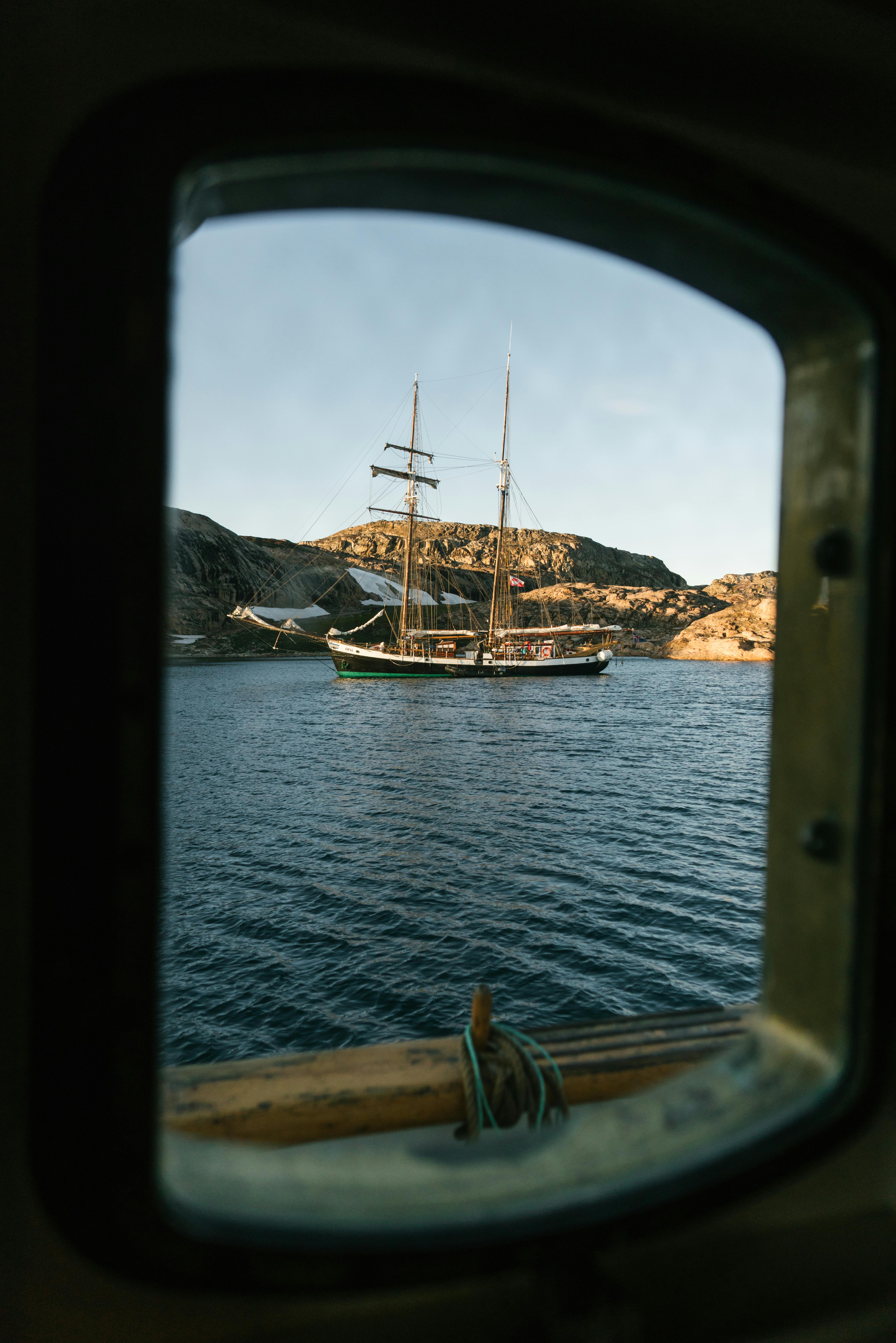 A tranquil view of a sailboat on the water framed by a cabin window at sunset.