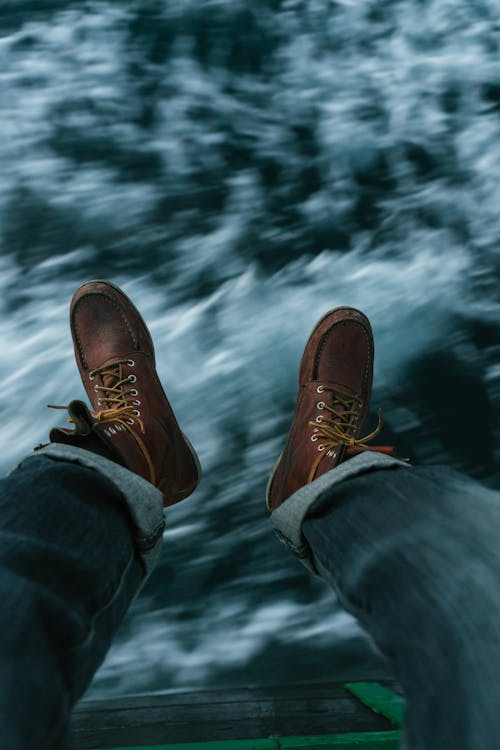 Free Sea Waves Beneath Person's Feet in Brown Leather Boots Stock Photo