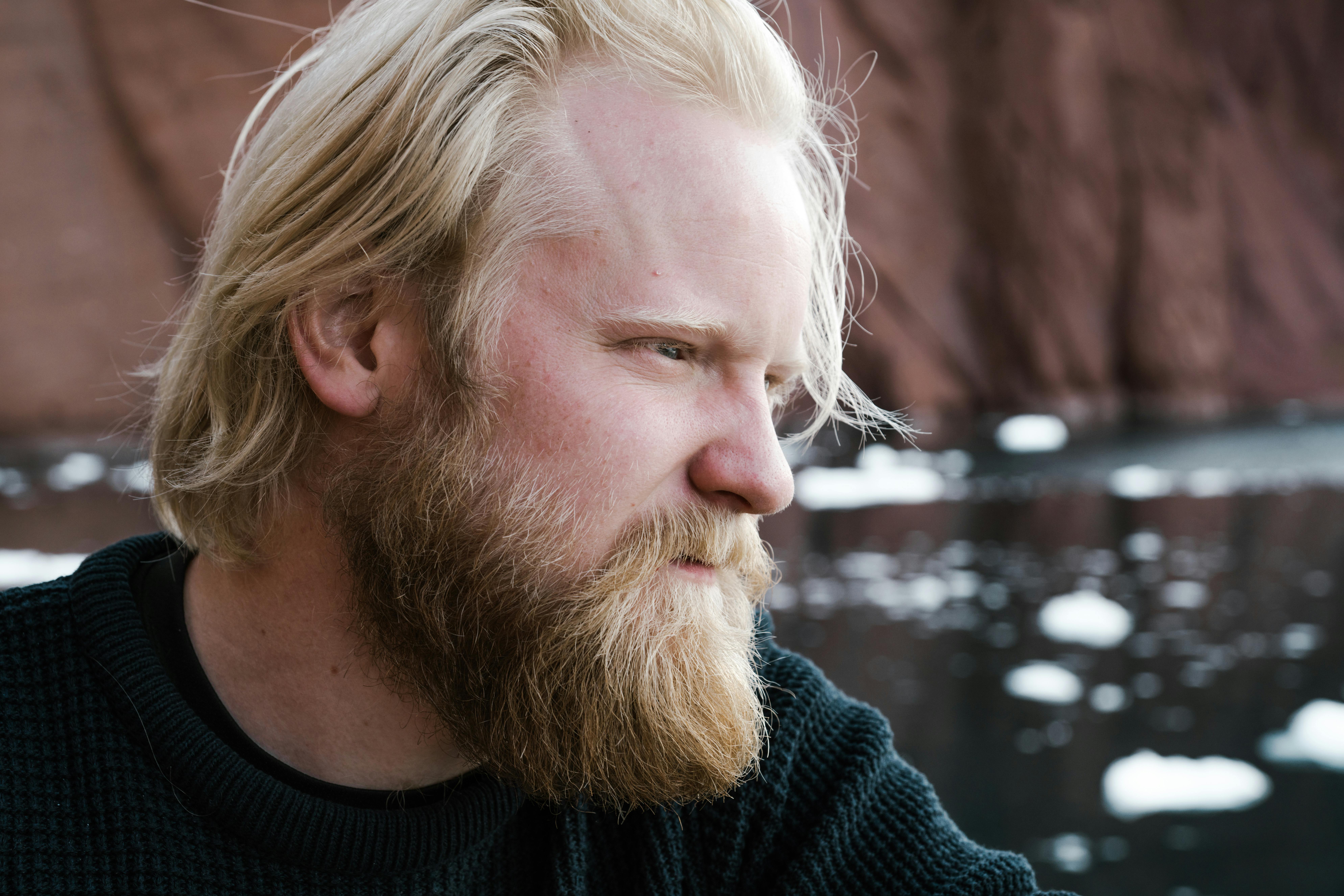 Side profile of a man with a beard gazing thoughtfully by a rocky lakeside.