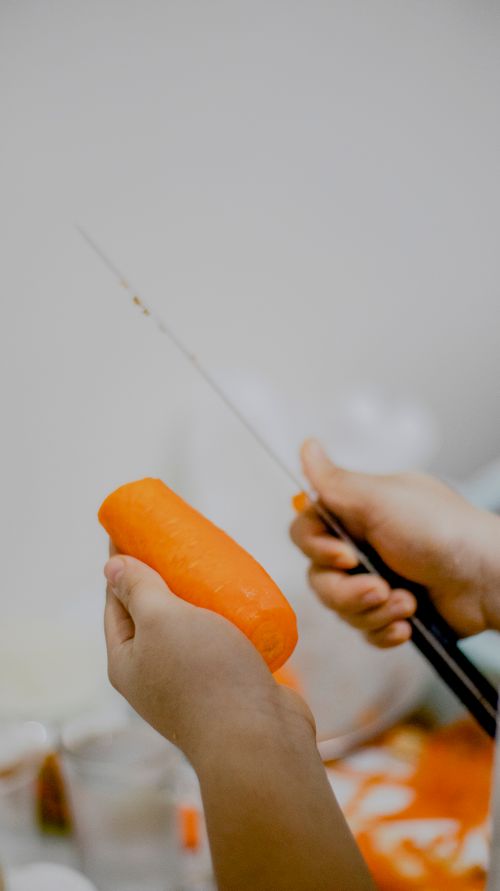 Free Hands preparing a fresh carrot using a sharp knife in a kitchen setting. Stock Photo