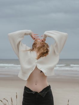 阴天，一位穿着白毛衣的女人在海边享受宁静的时刻