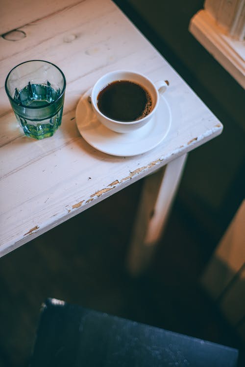 From above of ceramic cup of strong coffee near glass of water on shabby table in house