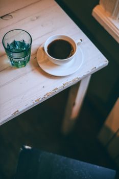 从破旧房子桌子上的陶瓷杯和浓咖啡旁，放着一杯水