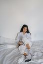 一位年轻女子身着白衣，随意地坐在室内的床上