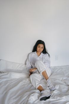 一位年轻女子身着白衣，随意地坐在室内的床上