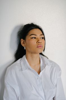 一位年轻而沉思的少数族裔女性，身着白衣，妆容精致，目光投向屋内