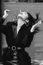 Black and white of trendy ethnic female in earrings with cigarette and closed eyes standing with head thrown back