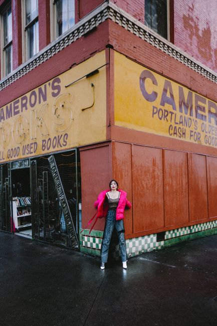 Young trendy ethnic female with bright makeup standing near wall of old urban book store