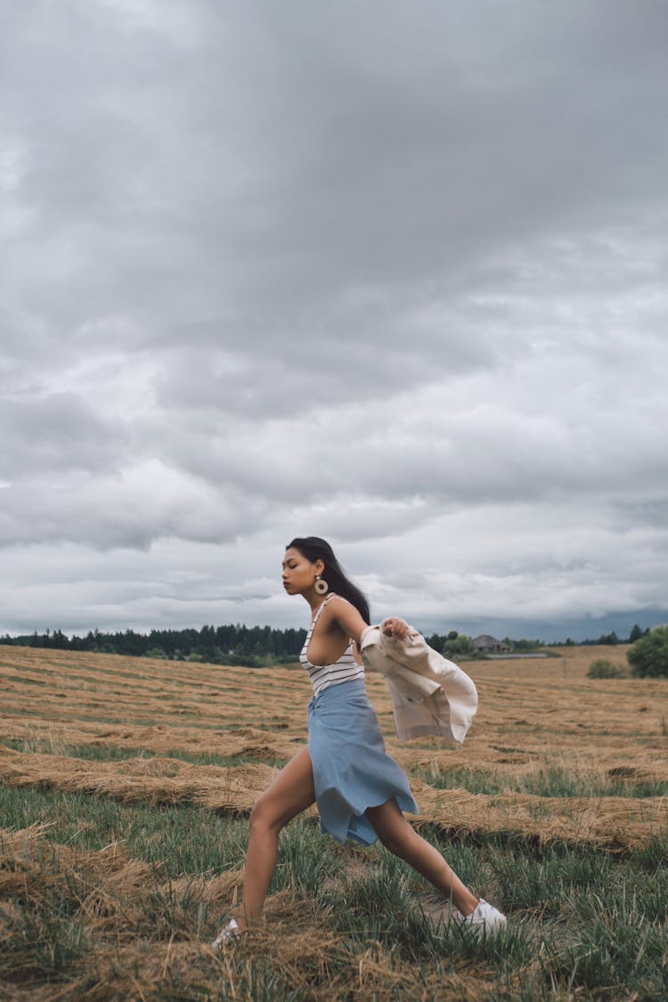 Ethnic Woman Running On Meadow Under Cloudy Sky