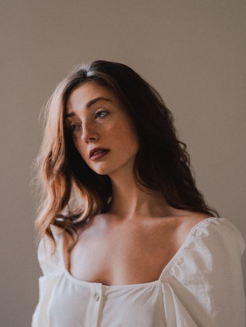 Young sensual dreamy female with makeup in white apparel looking away near wall