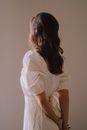 在柔和的灯光下，一名身穿别致白色连衣裙的女子在室内摆出背影姿势