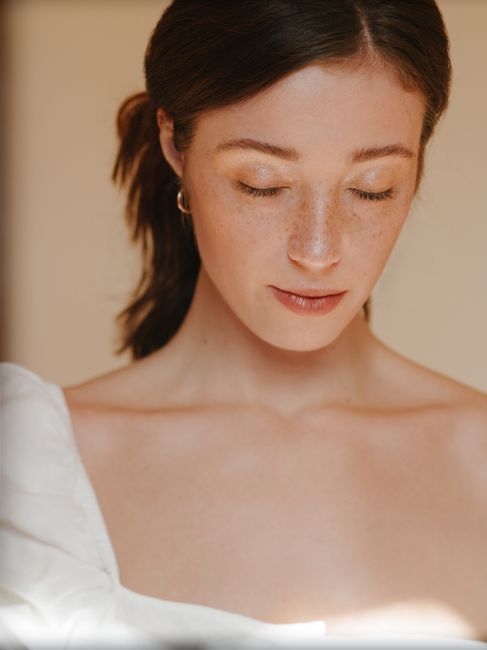 Crop tranquil calm female with freckles wearing white outfit standing with eyes closed against light wall