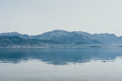 Picturesque view of spacious tranquil lake surrounded by hilly coast on foggy morning