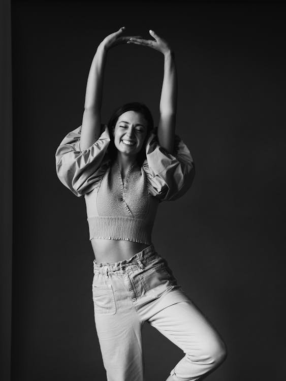 Cheerful smiling woman with eyes closed raising arms in studio