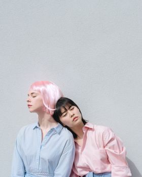Multiethnic female with modern hairstyles in trendy clothes leaning to each other with closed eyes