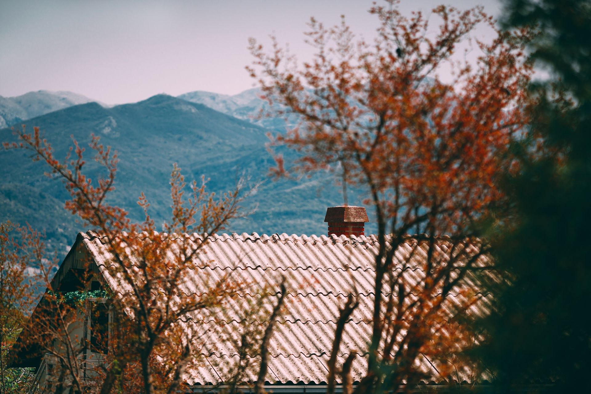 Exterior of residential building with red roof and chimney against rough rocky mountains in autumn