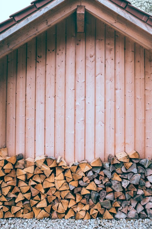 Exterior of structure with straight wooden walls and small dry logs on stony surface