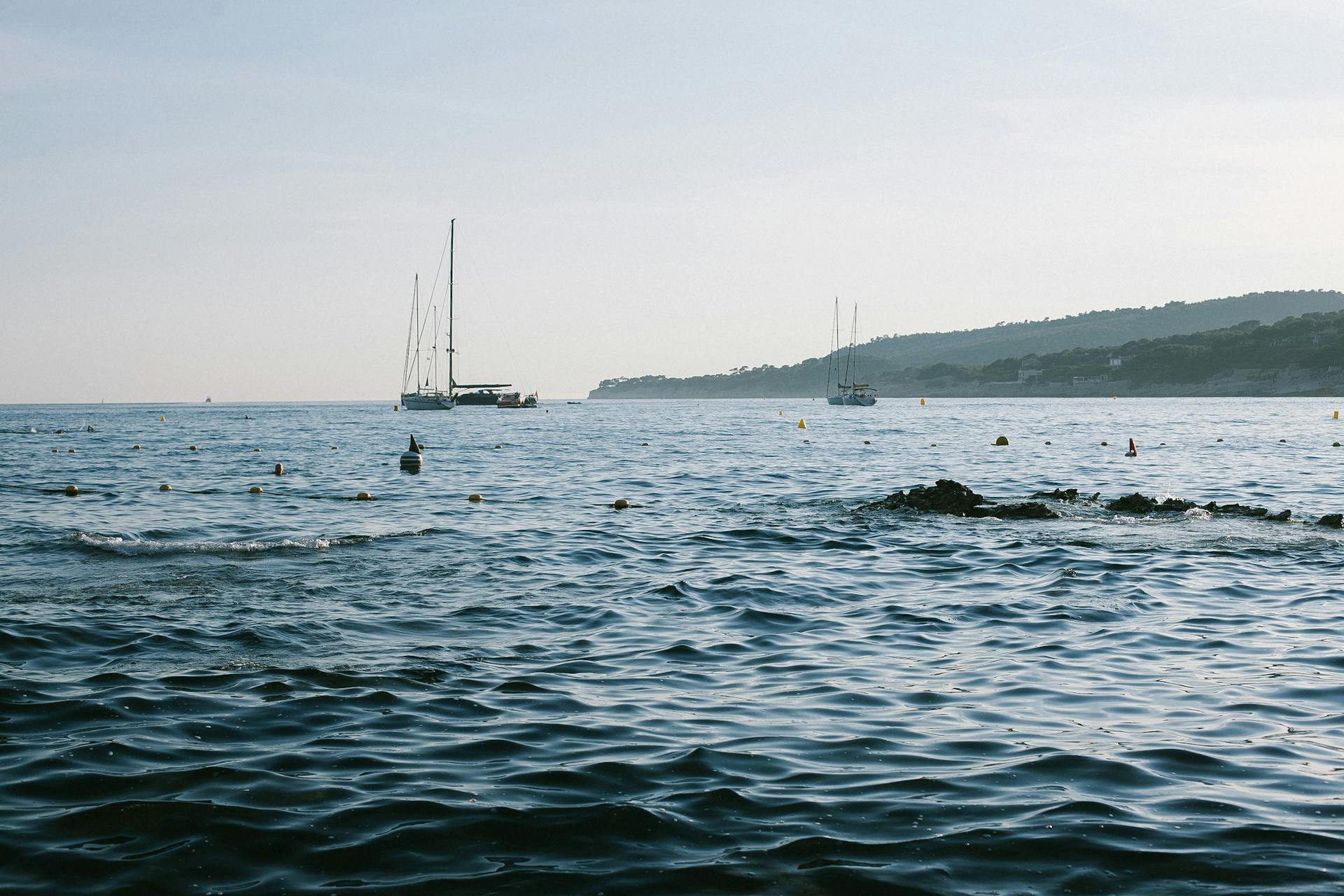 Picturesque scenery of wavy sea water with vessels near hill slope on coast