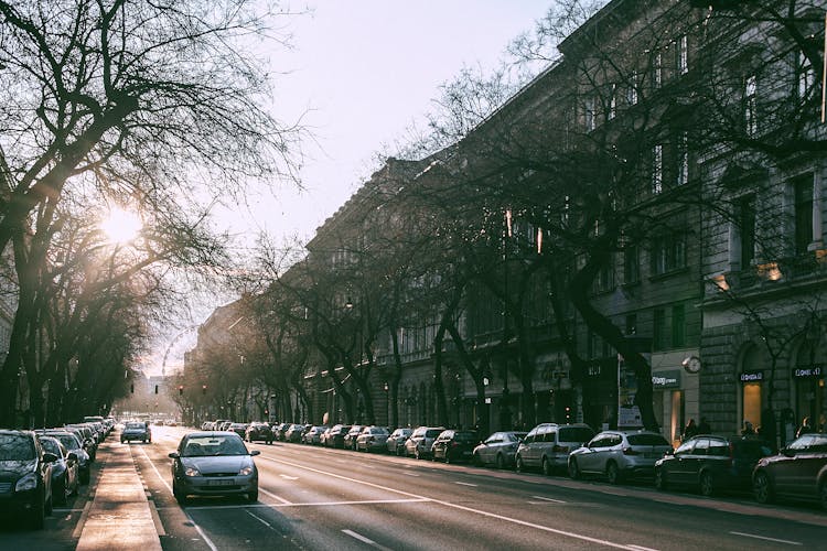 Wide Straight Road With Parked Cars In Cityscape On Sunny Morning