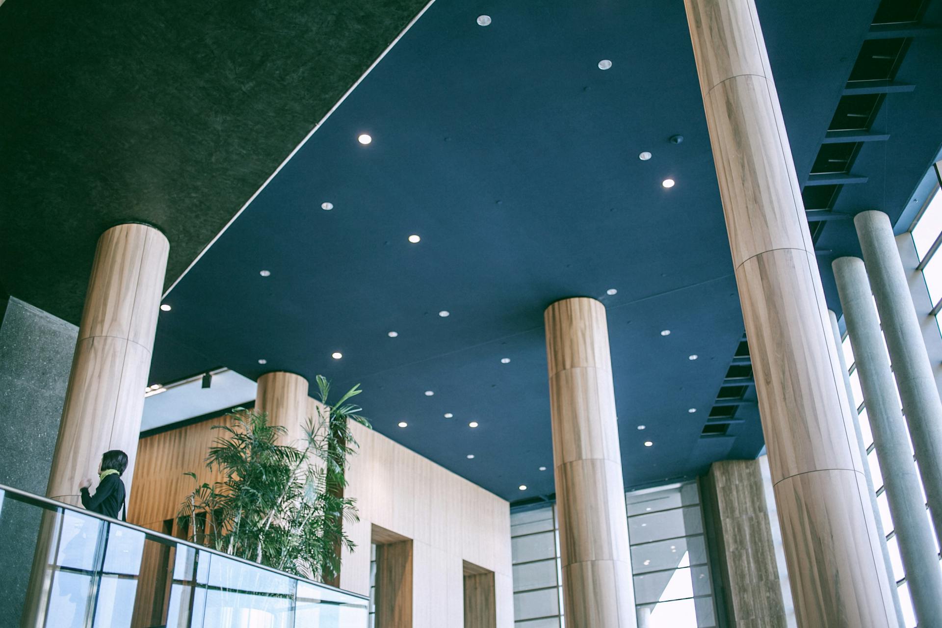 From below contemporary interior of spacious hall in business center with unusual columns and many  lamps on blue ceiling in sunlight