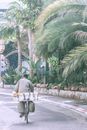 Anonymous man riding bicycle with box behind near palms