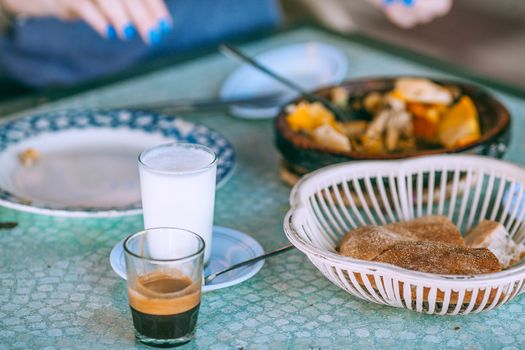 Person eating traditional food with milk and coffee in glasses at table in daylight