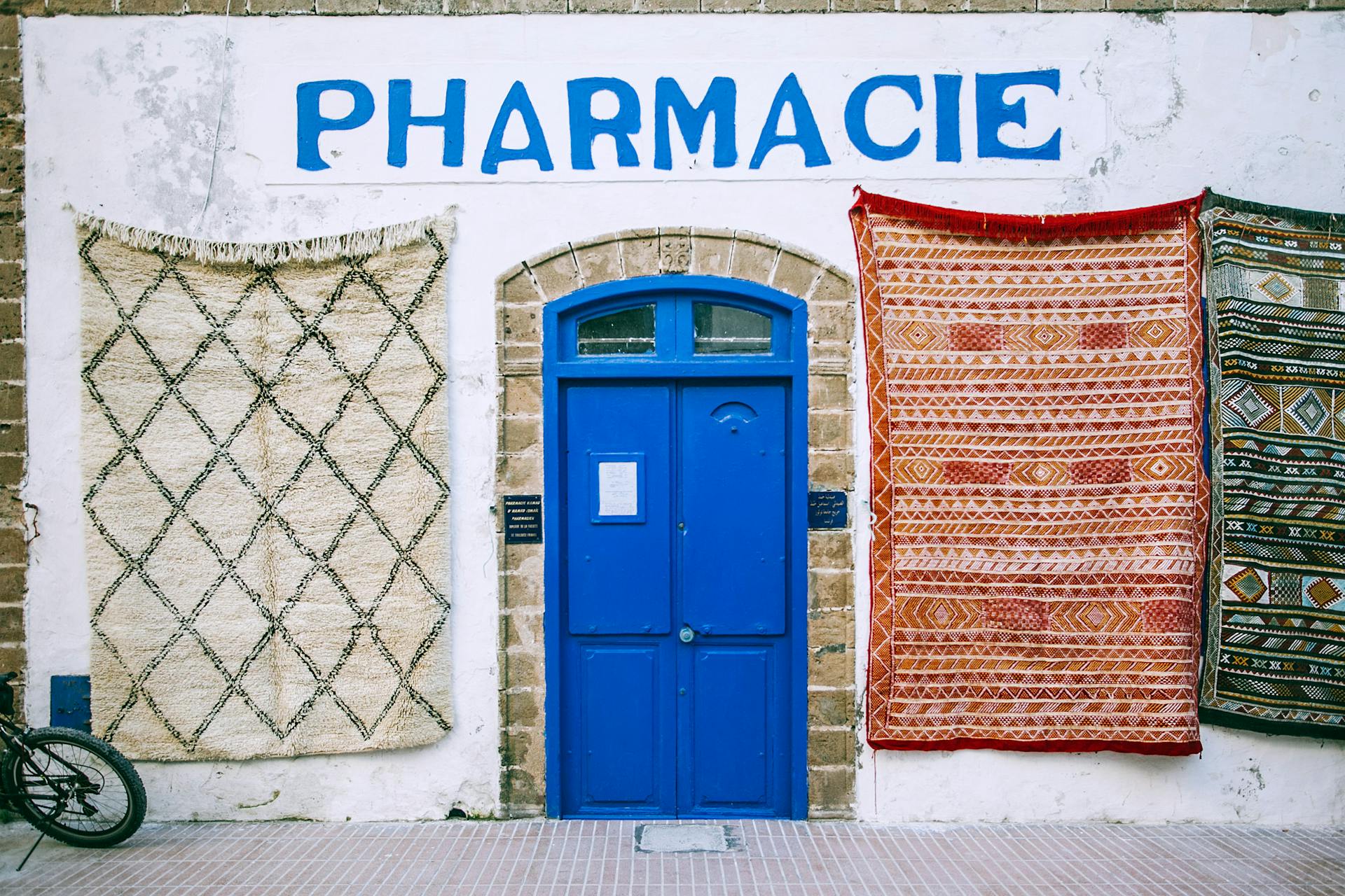 Facade of old pharmacy with bright blue doorway and oriental textile rugs on white shabby wall