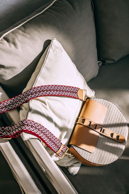 From above of trendy handbag with leather elements placed on gray sofa in sunny day