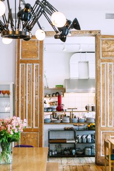 Comfortable furniture with flowers in vase and wooden arch in front of shelves with various utensils in modern kitchen