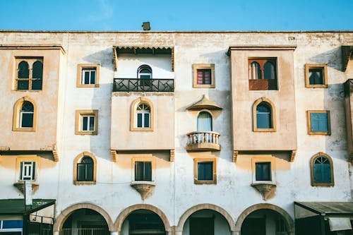 Exterior of aged dwell building with shabby facade and decorated windows with balconies over arches