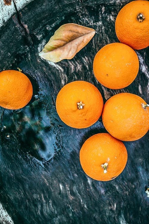 Top view of fresh orange tangerines and dry leaf on dark shabby tray