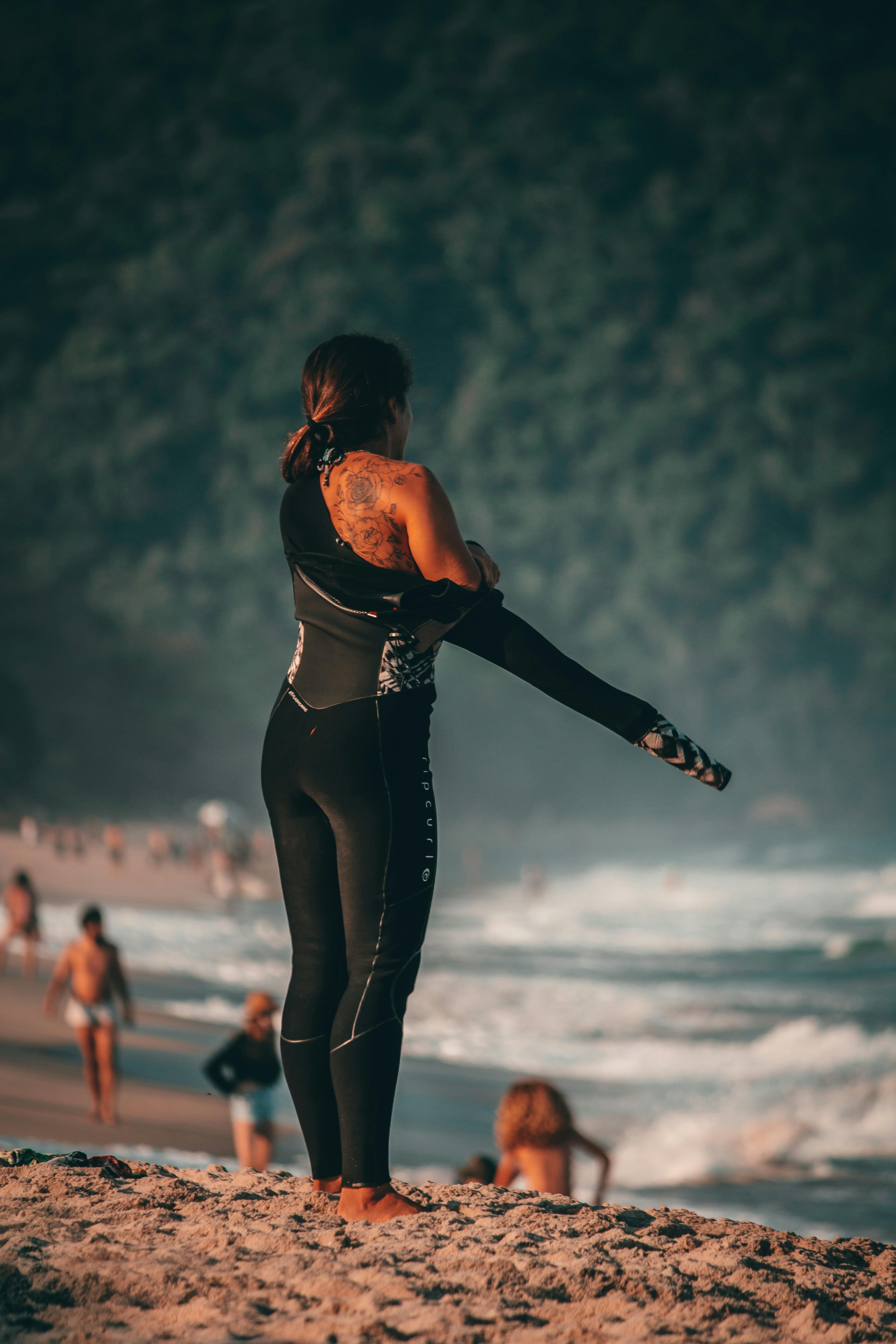 Woman in wetsuit getting ready to surf on a tropical beach with waves and lush backdrop.