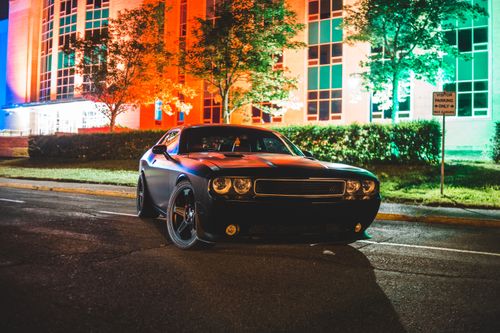 Free Shiny new automobile parked near modern building with green trees and bushes on lighted street Stock Photo